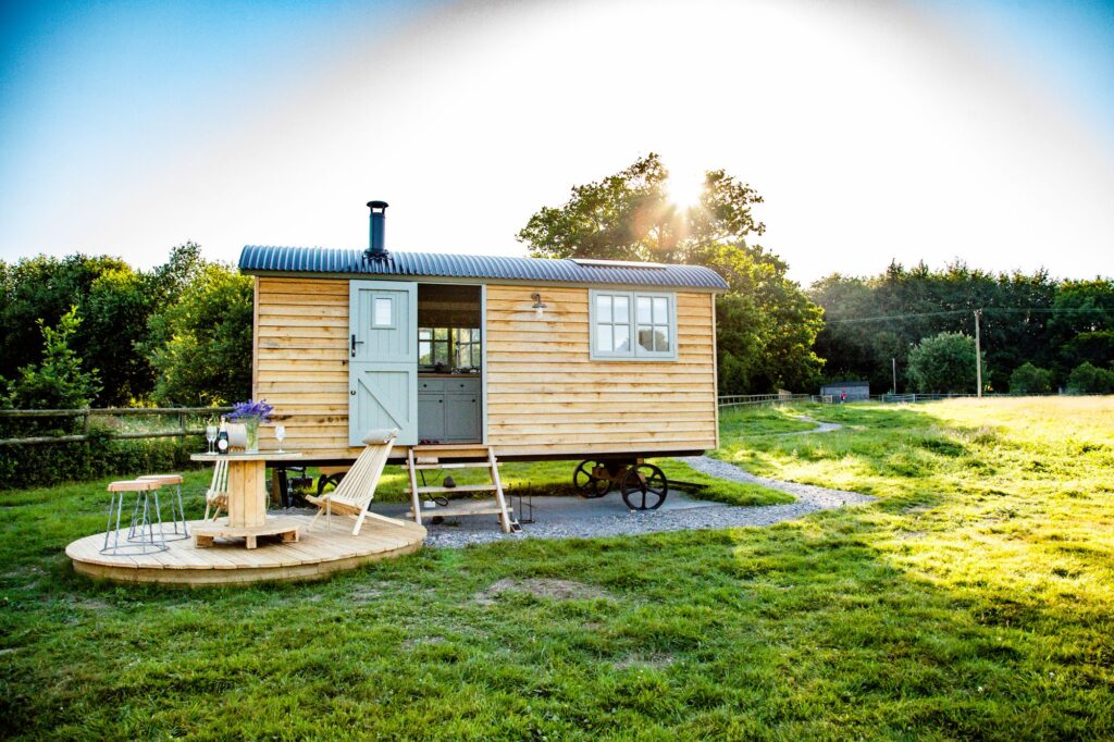 Shepherd's hut on filed with table with flowers and wine.